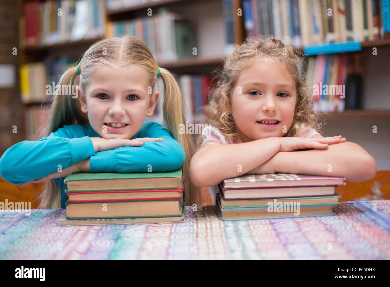 Cute pupils smiling at camera in library Stock Photo - Alamy