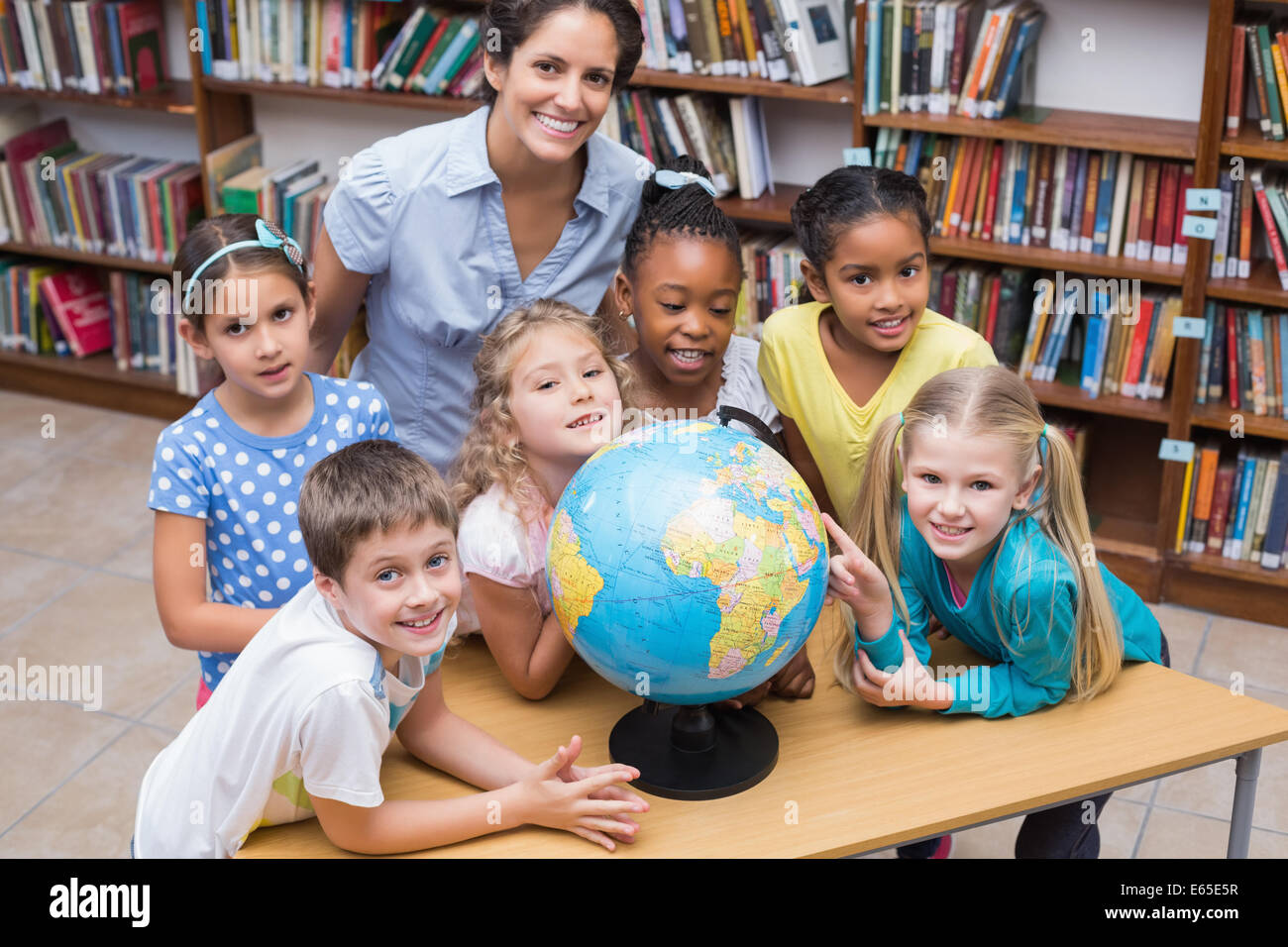 Cute pupils and teacher looking at globe in library Stock Photo - Alamy