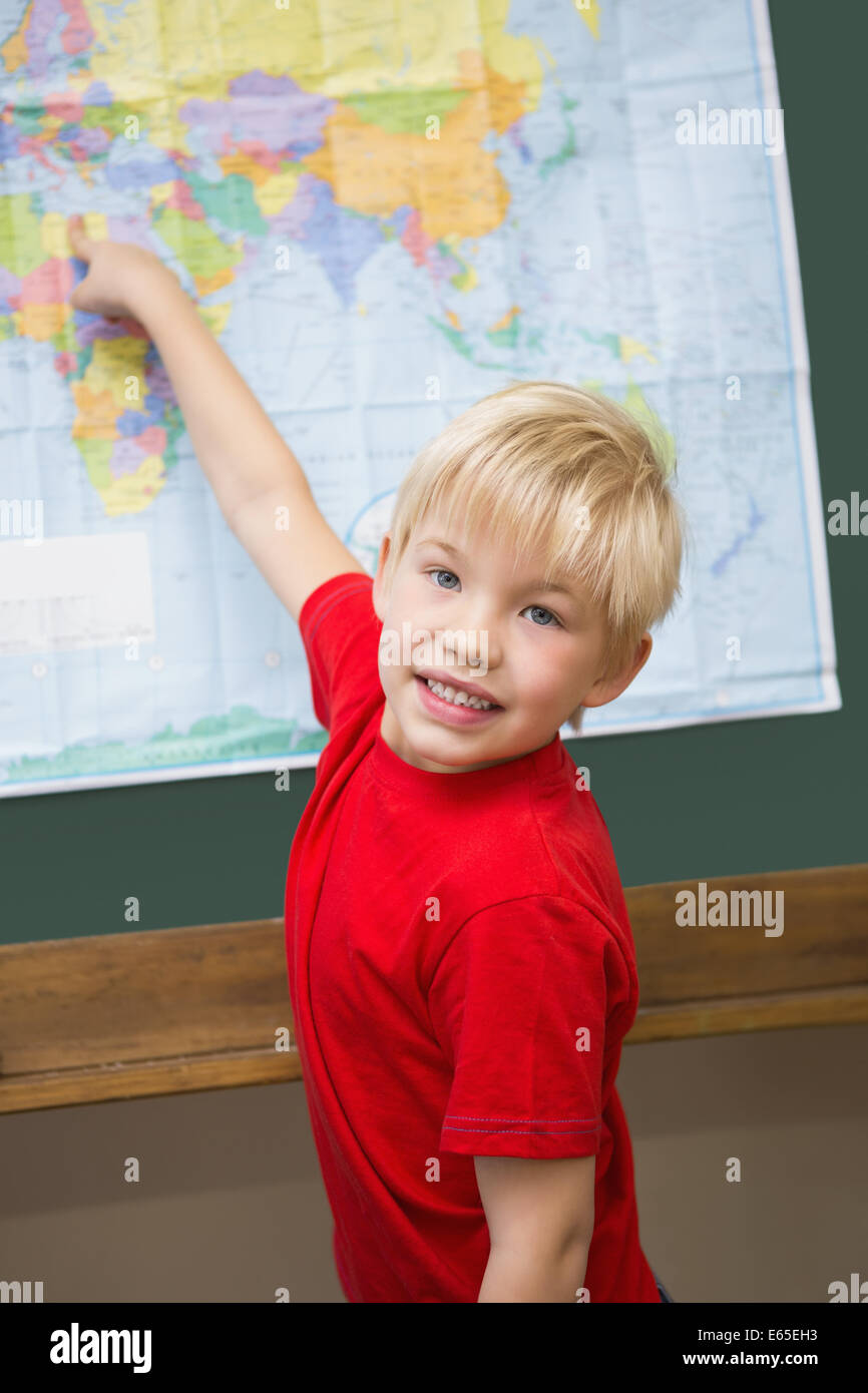 Cute pupil smiling at camera in classroom pointing to map Stock Photo ...