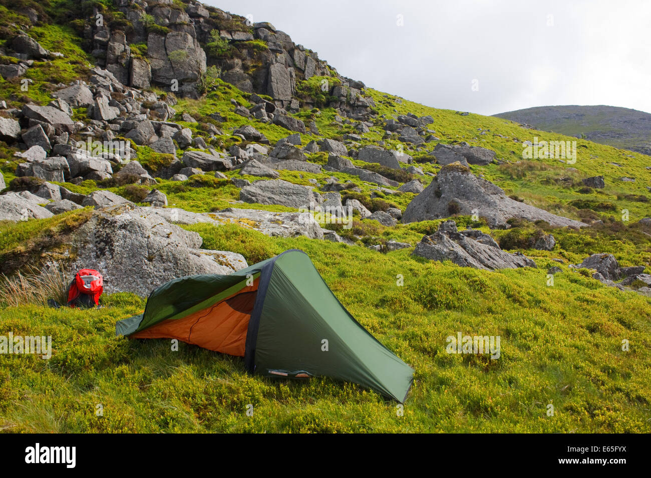 A tent pitched in a wild campsite in the mountains below a rocky slope Stock Photo