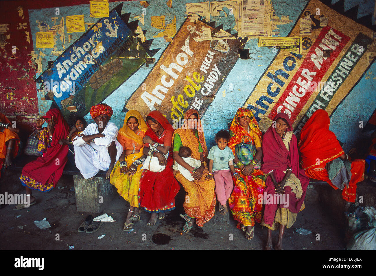 Tribespeople belonging to the Bhil community are waiting for a bus in a bus station. On the wall, there are advertisements. Stock Photo