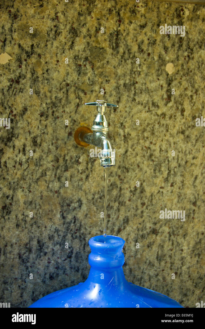 Water Tap dropping just a little bit of water to fill the big blue bottle Stock Photo