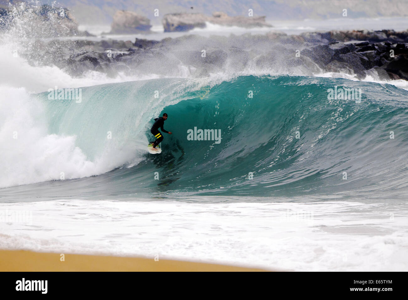 A local surfer pulls into a heavy, shore breaking barrel in shallow water at the surf break The Wedge, in Newport Beach, CA Stock Photo