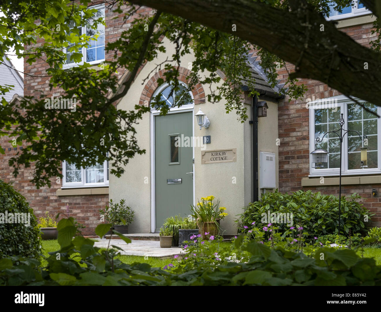 Attractive modern cottage style house front door and porch seen through trees, Leicestershire, England, UK. Stock Photo