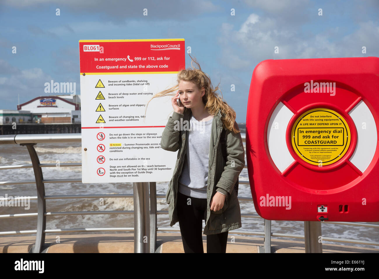 Teenage girl using mobile phone to call the coastguard emergency service on the seafront at Blackpool Lancashire England UK Stock Photo