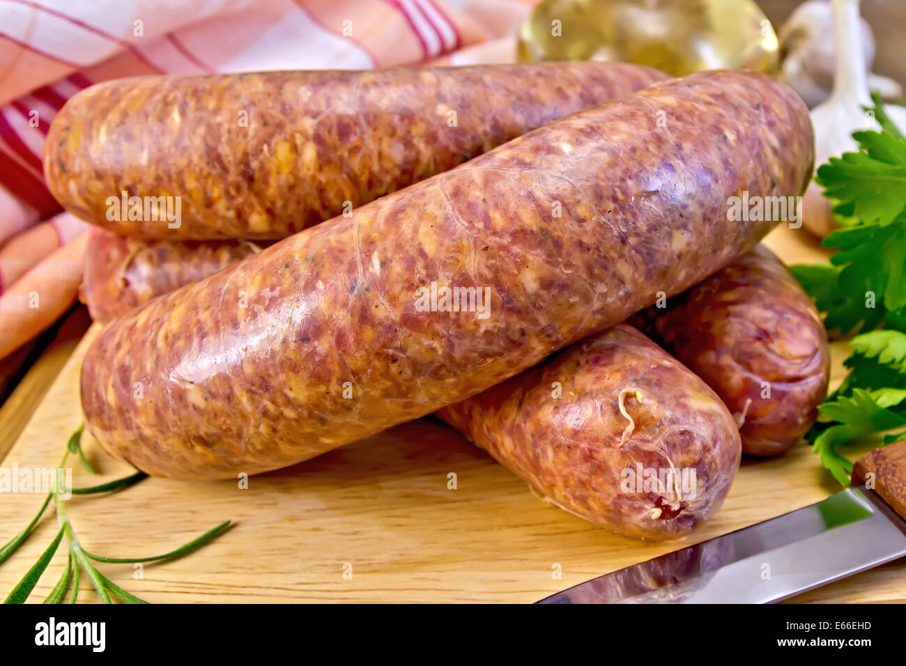 Raw beef sausage, knife, rosemary, parsley, vegetable oil and a napkin on the background of wooden boards Stock Photo