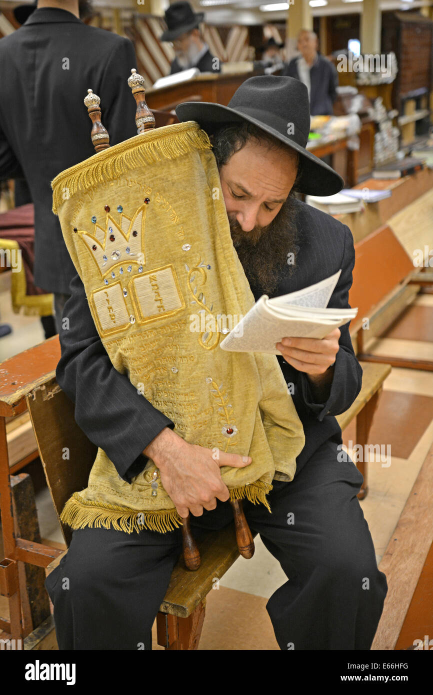 Religious Jewish man praying while holding a Torah during Tisha B'Av services in a synagogue in Brooklyn, New York, USA Stock Photo