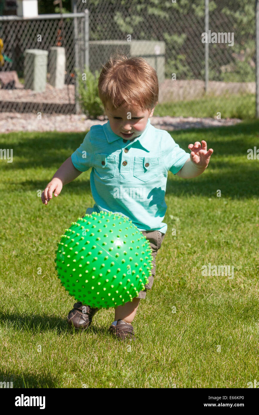 Toddler Playing with Green Plastic Ball in Backyard, USA Stock Photo