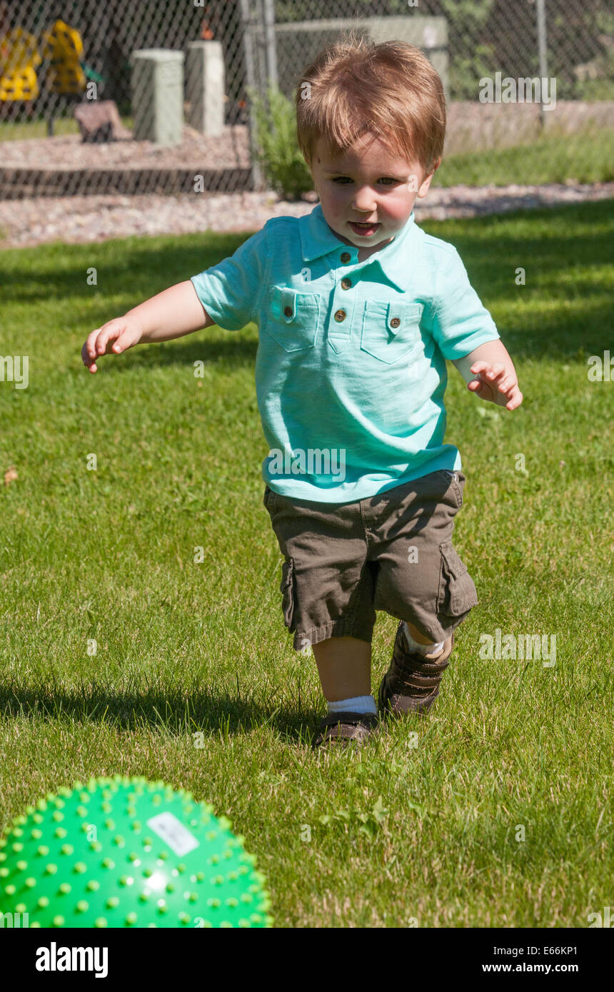 Toddler Playing with Green Plastic Ball in Backyard, USA Stock Photo