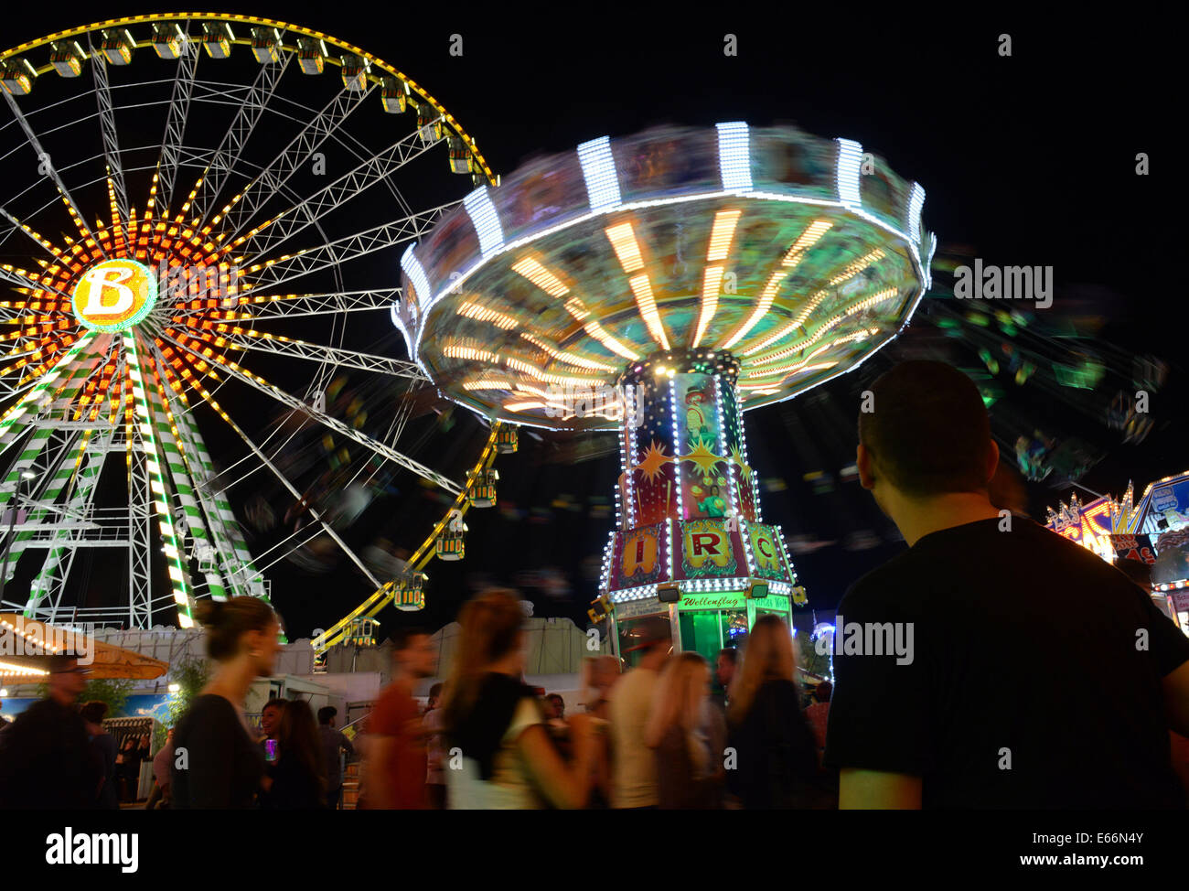 Herne, Germany. 9th Aug, 2014. Visitors walk past an illuminated chairoplane and a ferris wheel across the grounds of the Cranger fun fair in Herne, Germany, 9 August 2014. Photo: Caroline Seidel/dpa/Alamy Live News Stock Photo