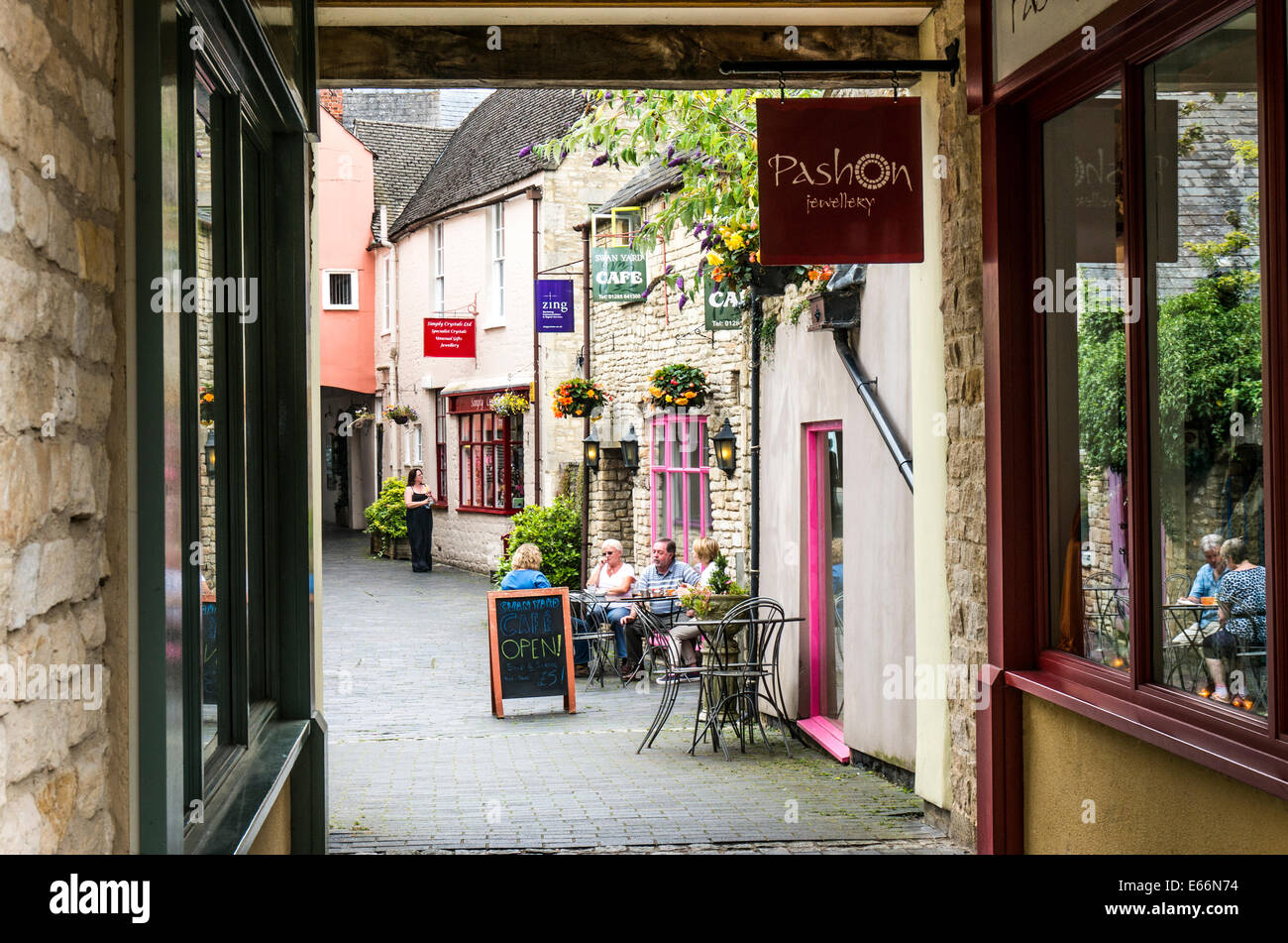 People sitting outside a cafe, with other independent shops, in a quant side street of Cirencester town, Cotswolds, Gloucestershire, England, UK. Stock Photo