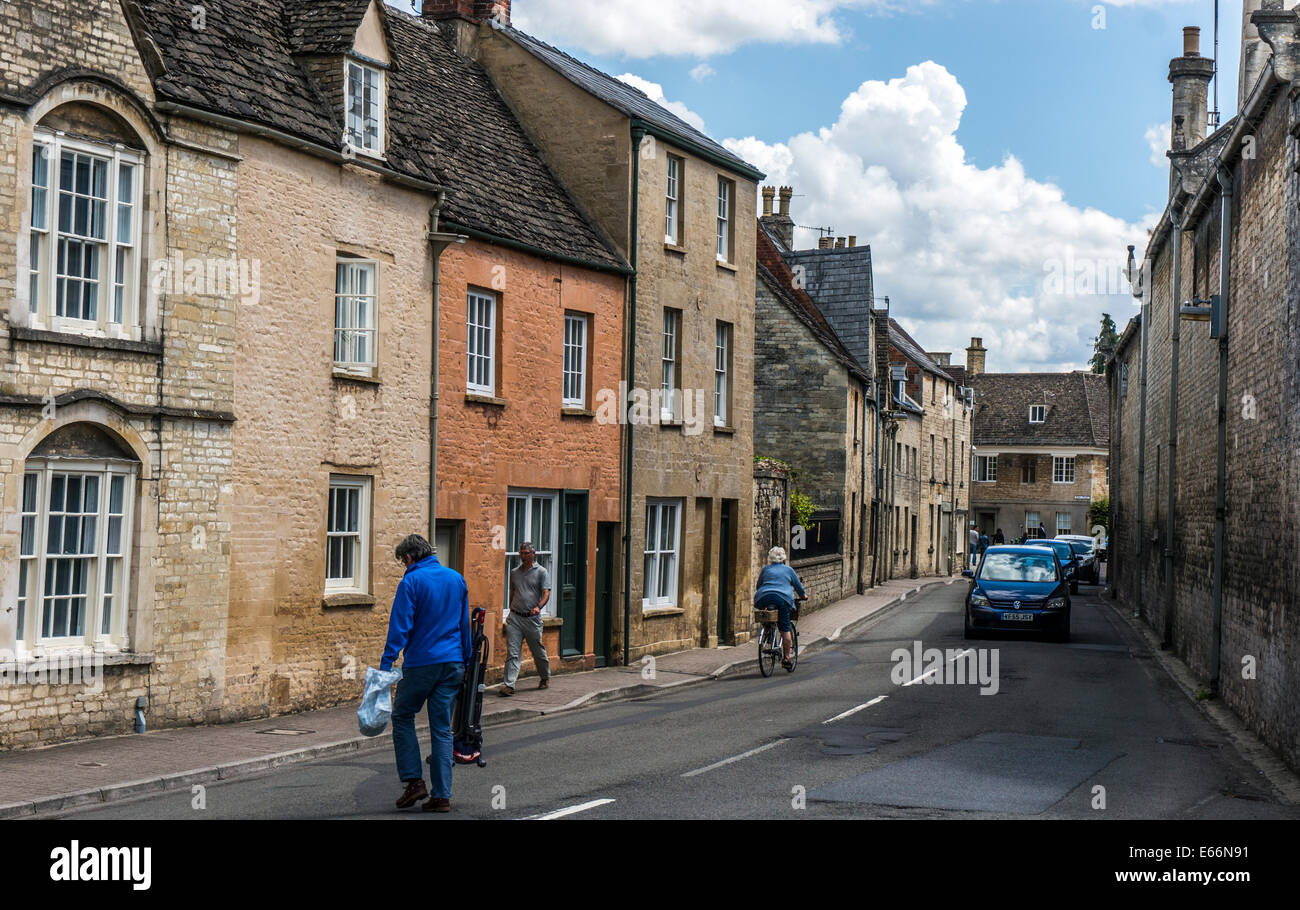 Picturesque street scene of an old lady on a bike, pedestrians and period houses, Cirencester town centre, Cotswolds, Gloucestershire, England, UK. Stock Photo