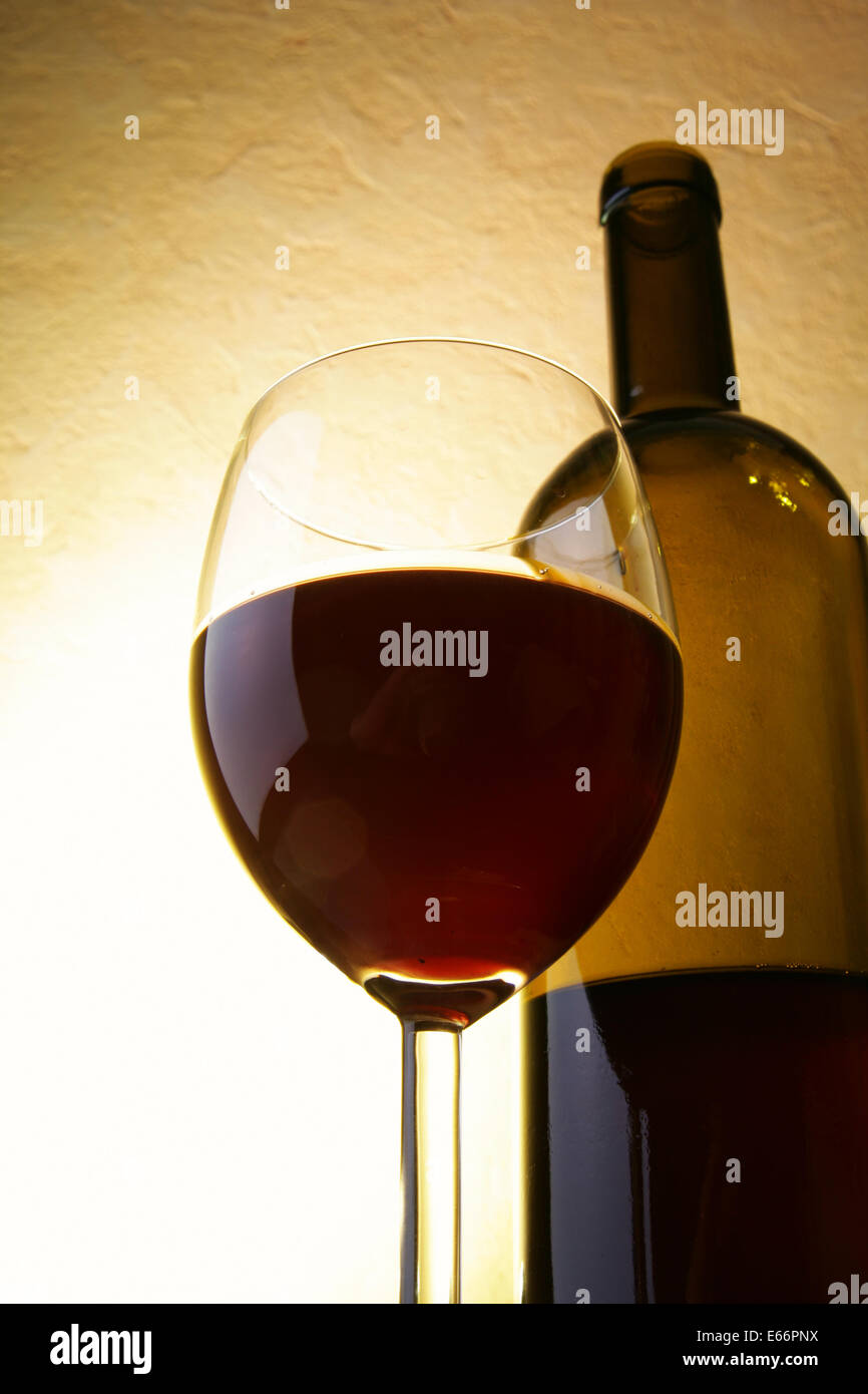 Glass of red wine and bottle close up over yellow background Stock