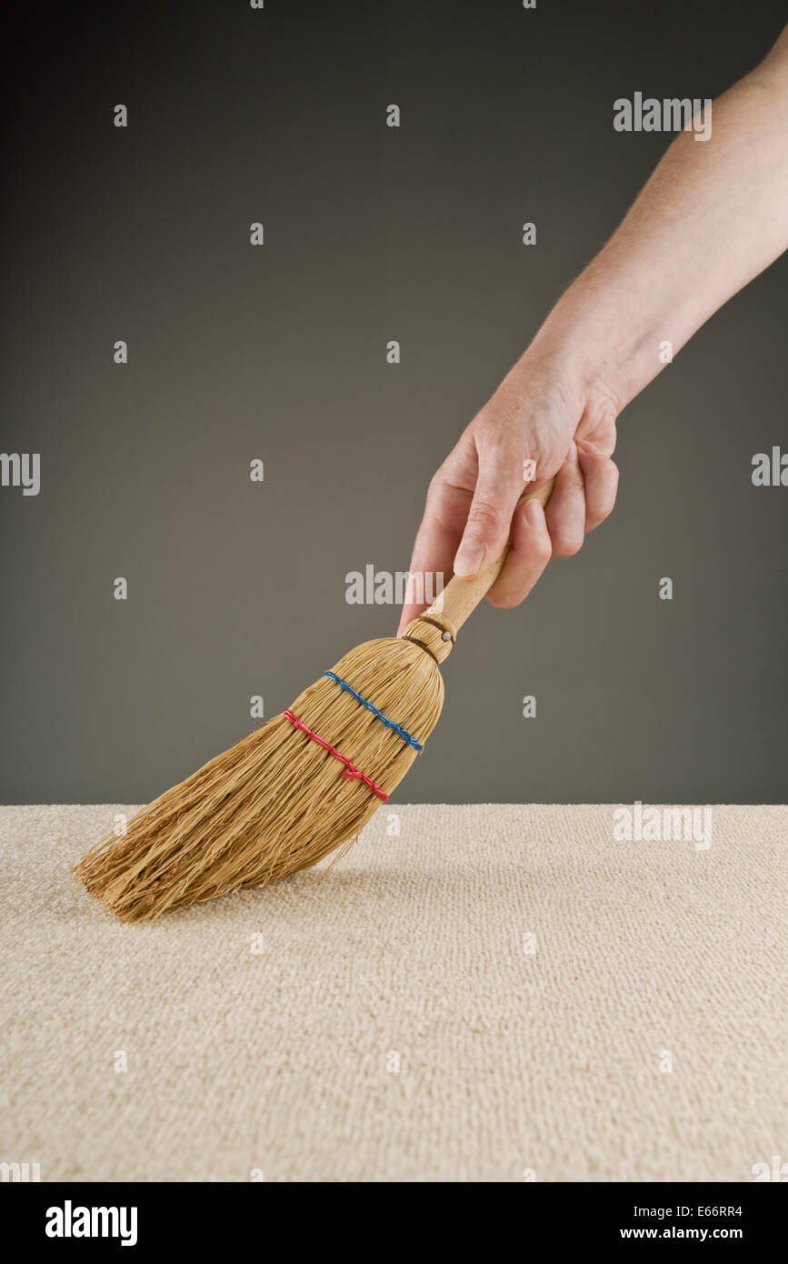 Female hand is sweeping carpet with short handle broom. Housewife in action. Stock Photo