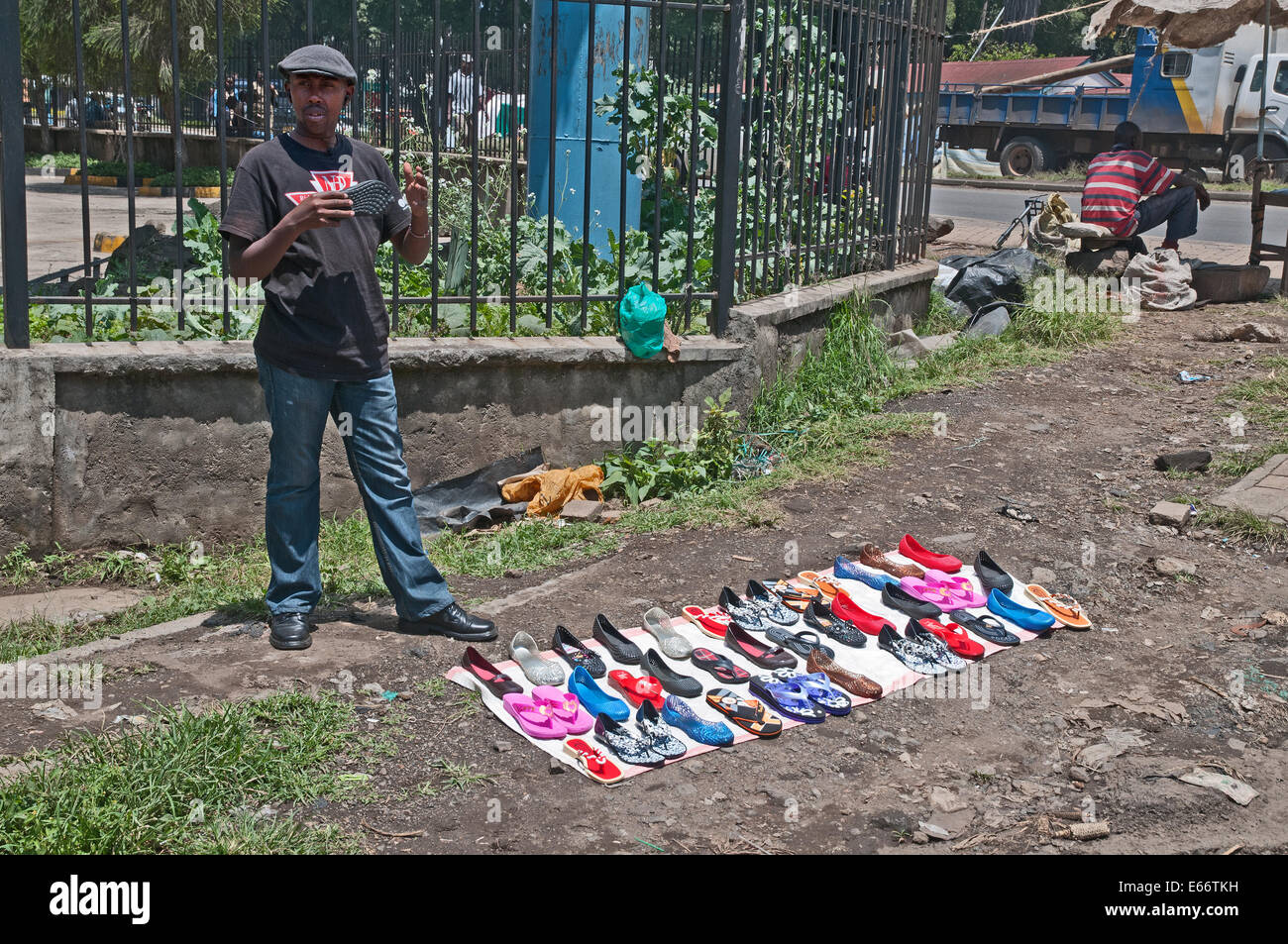 Man trying to sell shoes footware flip flops at side of road with shoes displayed on piece of cloth Stock Photo