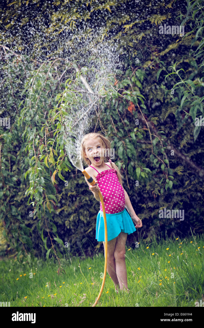 Young girl playing with water and hosepipe in the garden Stock Photo