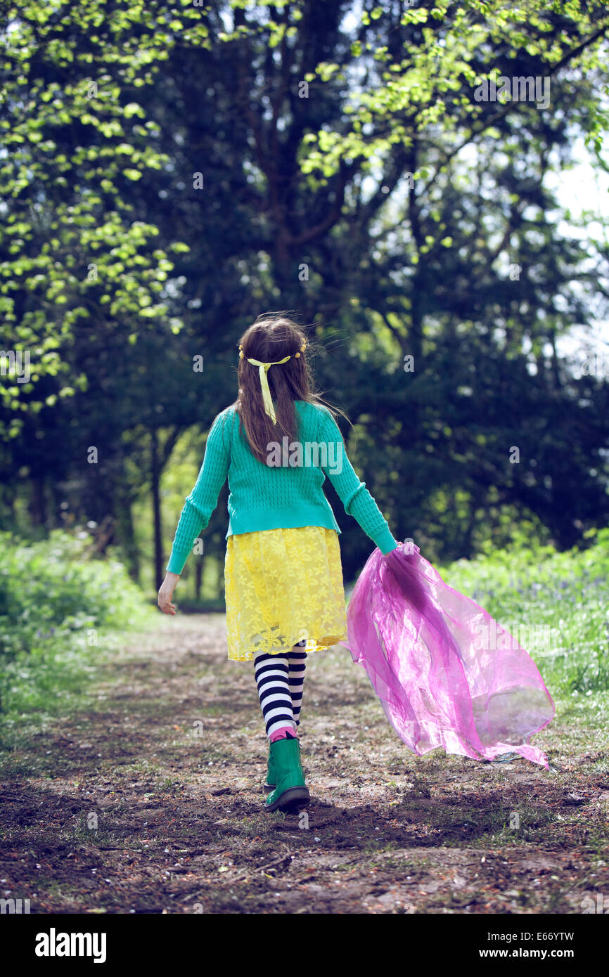 Young girl in brightly coloured dress, walking along a path through an English woodland. Stock Photo