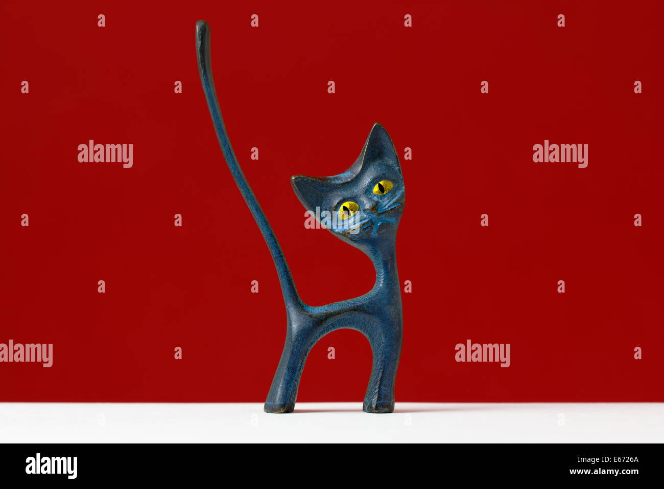 Figurine of a weird cat with cartoon like eyes and long tail on red background. Stock Photo