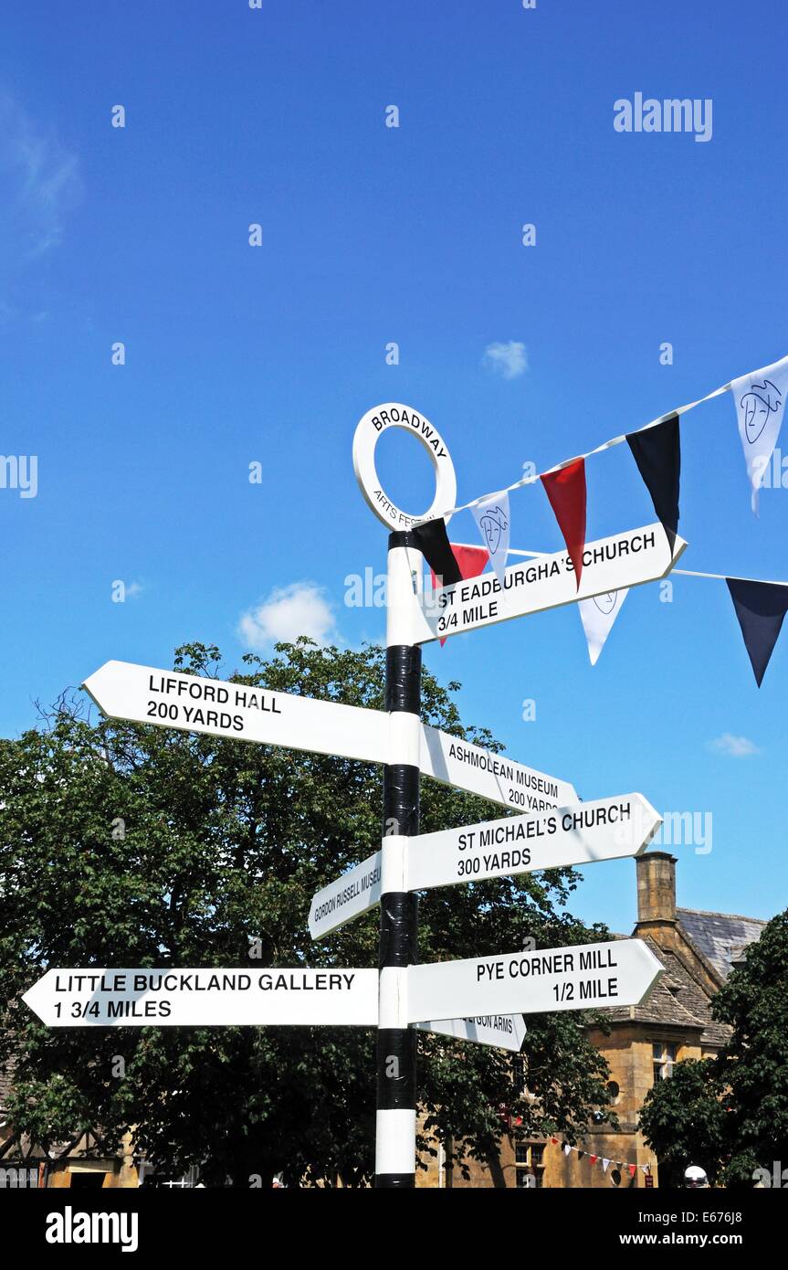 Black and white signpost on the village green along the High Street giving directions to tourist attractions, Broadway, UK. Stock Photo