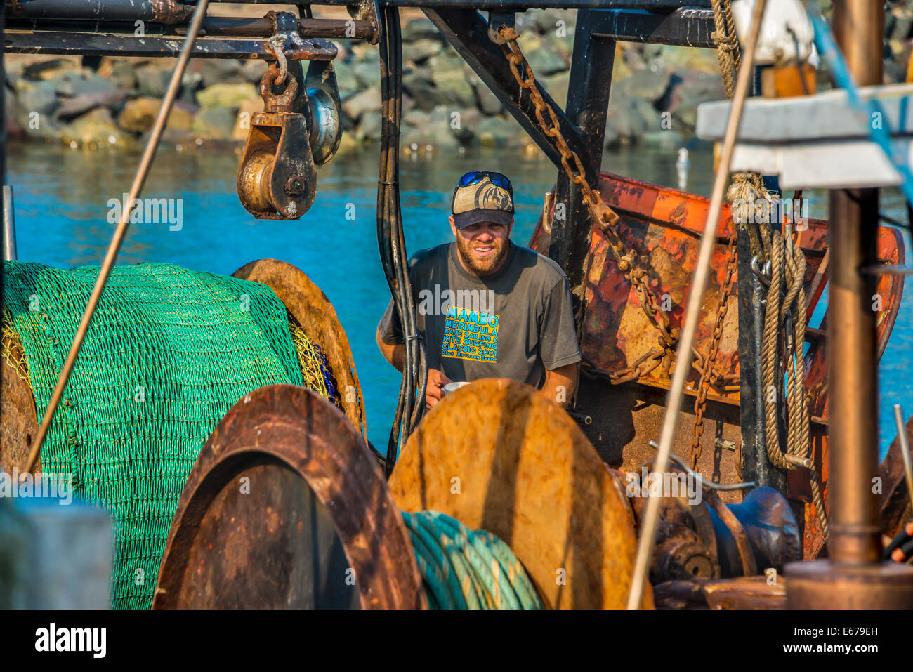 Man working on fishing boat with heavy fishing boat equipment, rusted and weathered chains ropes and nets with pulley system Stock Photo