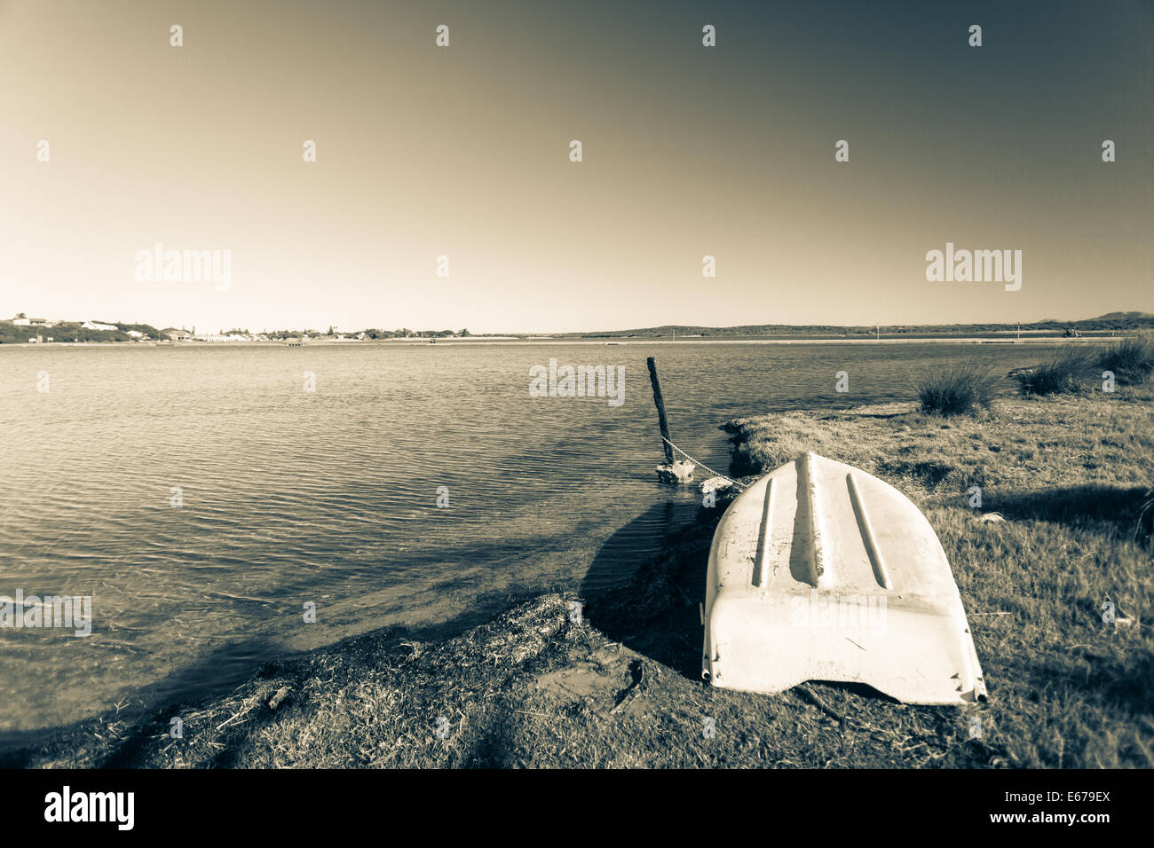 Boat upside down abandoned next to large river lagoon in vintage sepia landscape Stock Photo