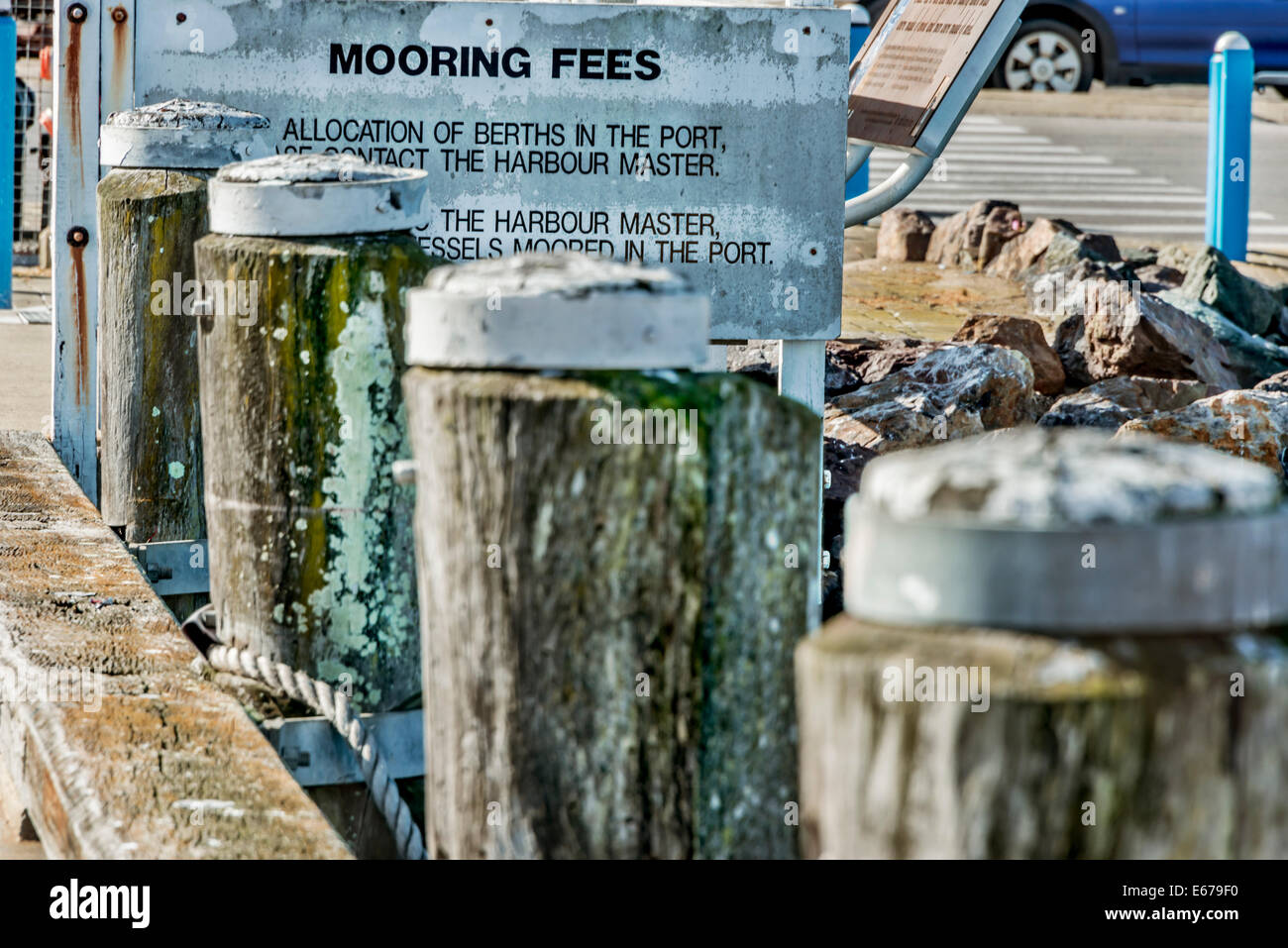 Old weathered wooden mooring posts, with mooring fees sign on Eden Wharf, Eden, NSW Australia Stock Photo