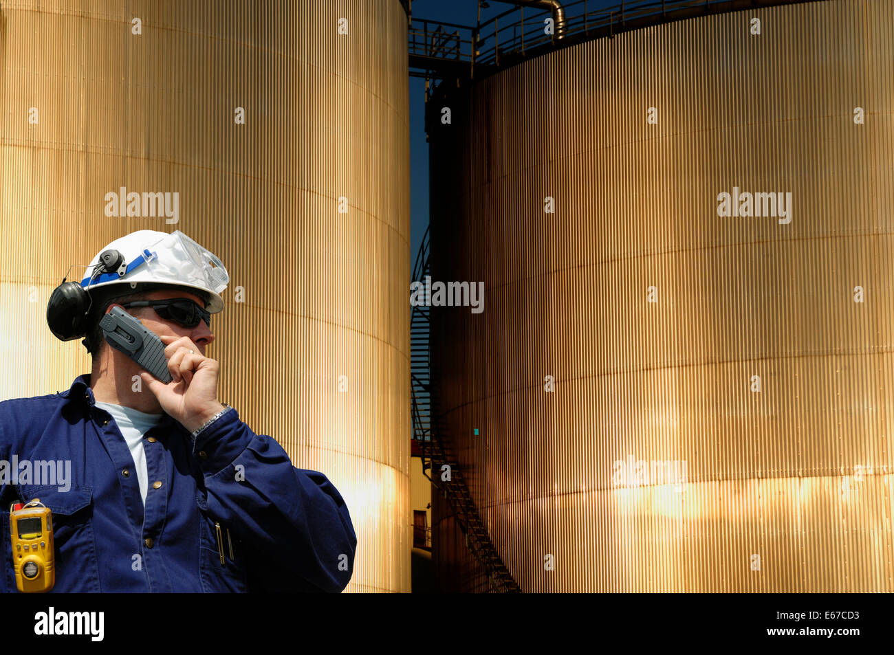 engineer, worker with fuel storage tanks in background, sunset, early ...