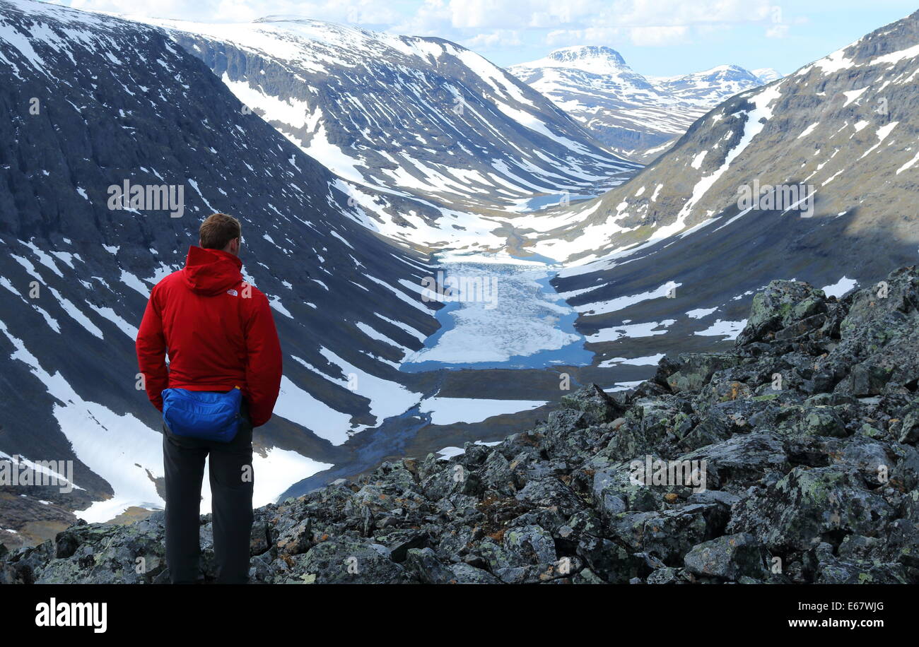 Walker in brightly coloured outdoor gear admires the view on the Kungsleden hiking trail in Sweden. Stock Photo