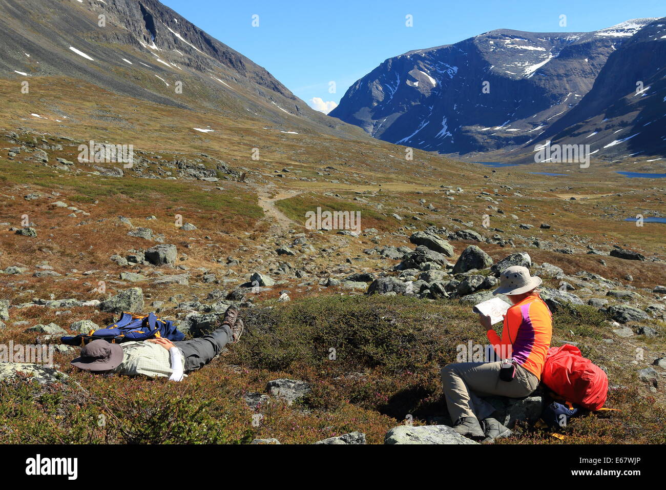 Walkers in brightly coloured outdoor gear rest and read a map on the Kungsleden hiking trail in Sweden. Stock Photo