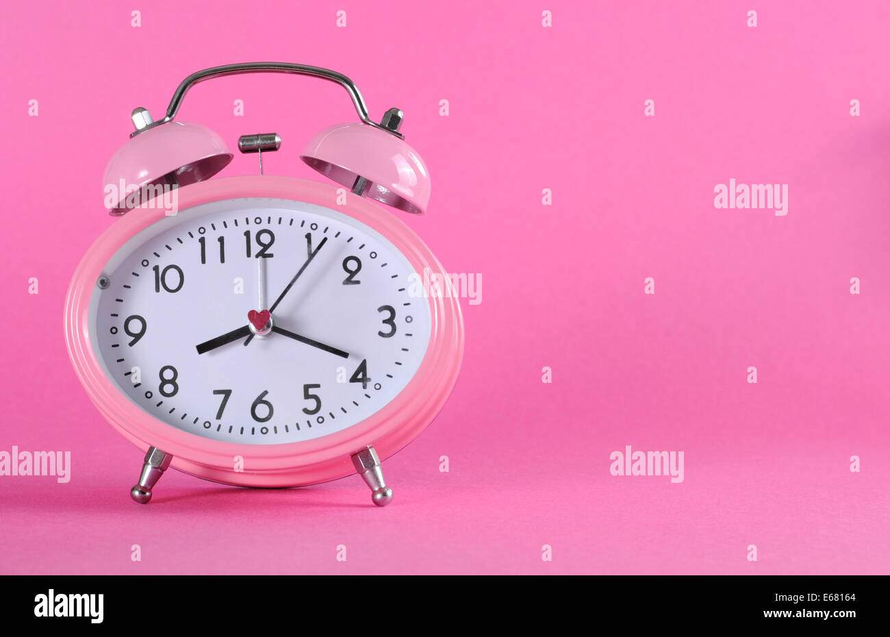 Pretty pink vintage retro style alarm clock with copy space on pink background for daylight saving, time keeping. Stock Photo