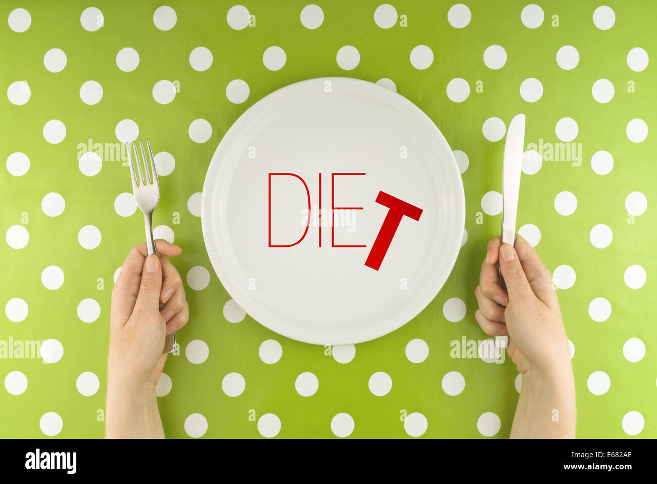 Female hands at dinner table holding fork and a knife above plate as dieting concept. Word Diet becoming Die reffering to health Stock Photo