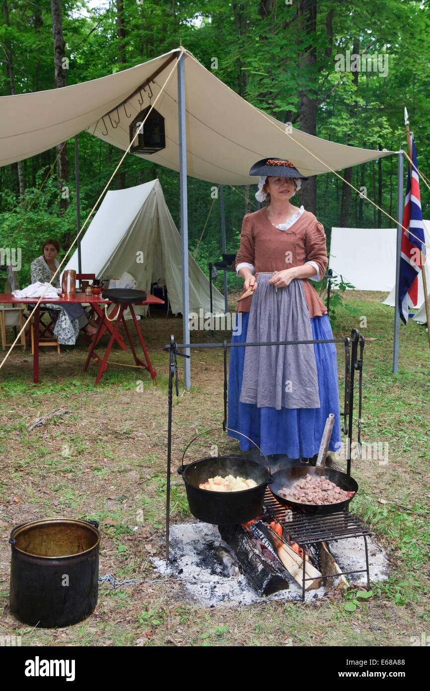 Woman cooking dinner over campfire in American Revolutionary war reenactment campsite Stock Photo
