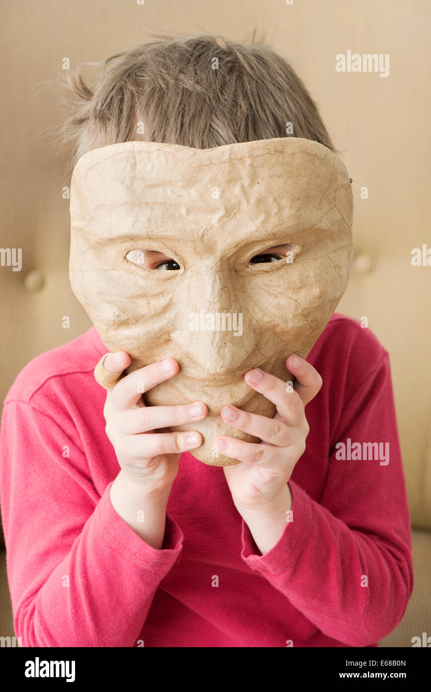 Sad little girl hiding face behind happy mask Stock Photo