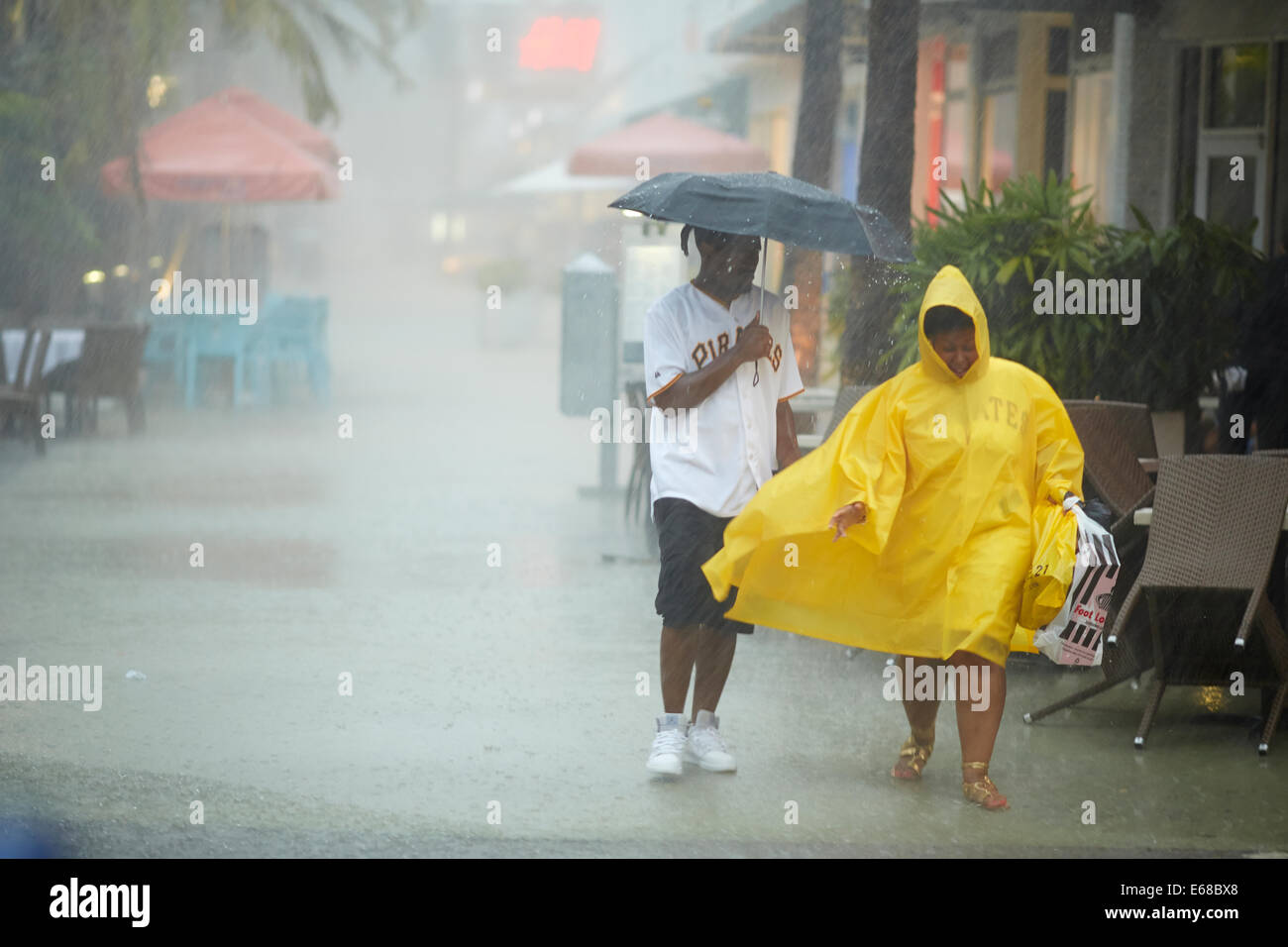 A man holding an umbrella and a woman wearing a rain coat to keep themselves out the rain storm Stock Photo