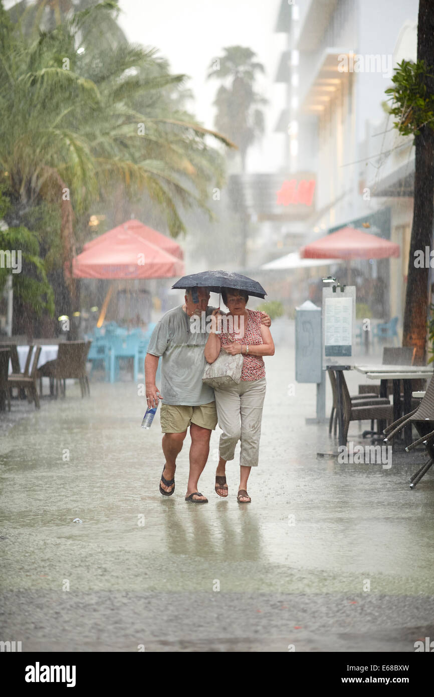 Elderly couple shelter under a umbrella to keep out of tropical storm in Miami, Florida. Stock Photo