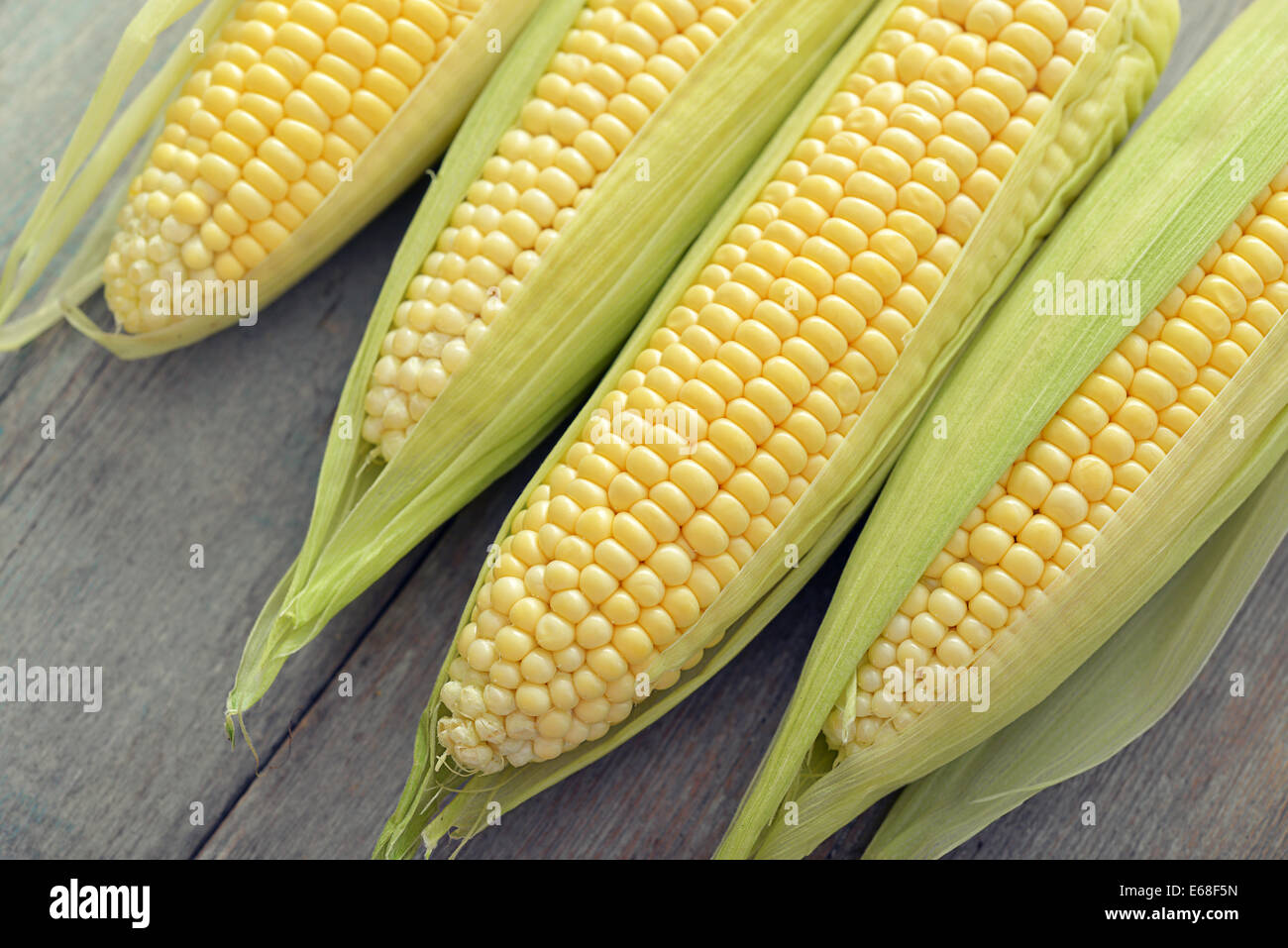 Raw corn cobs on wooden background closeup, top view Stock Photo