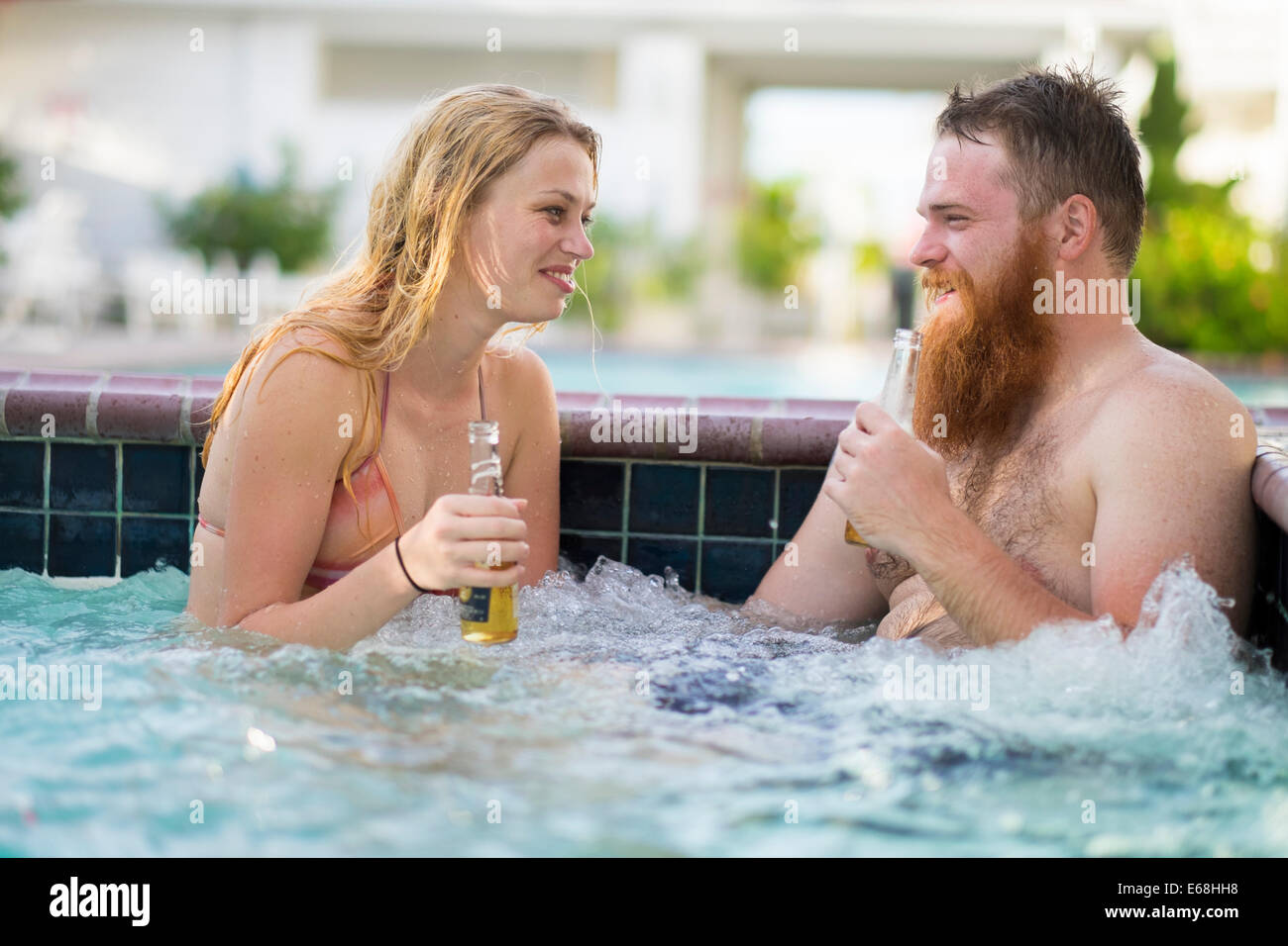 Young woman and a man sitting in hot tub pool with bubbling water while drinking beer. Stock Photo