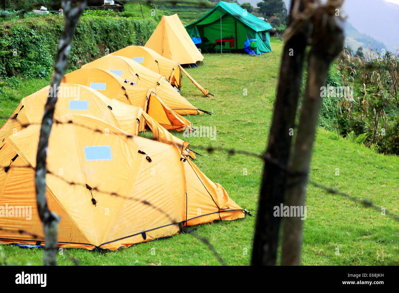 Yellow tents of a campsite laided on a terraced field at the foot of Lali Gurans Guest house closed by a barbed wire fence. Land Stock Photo