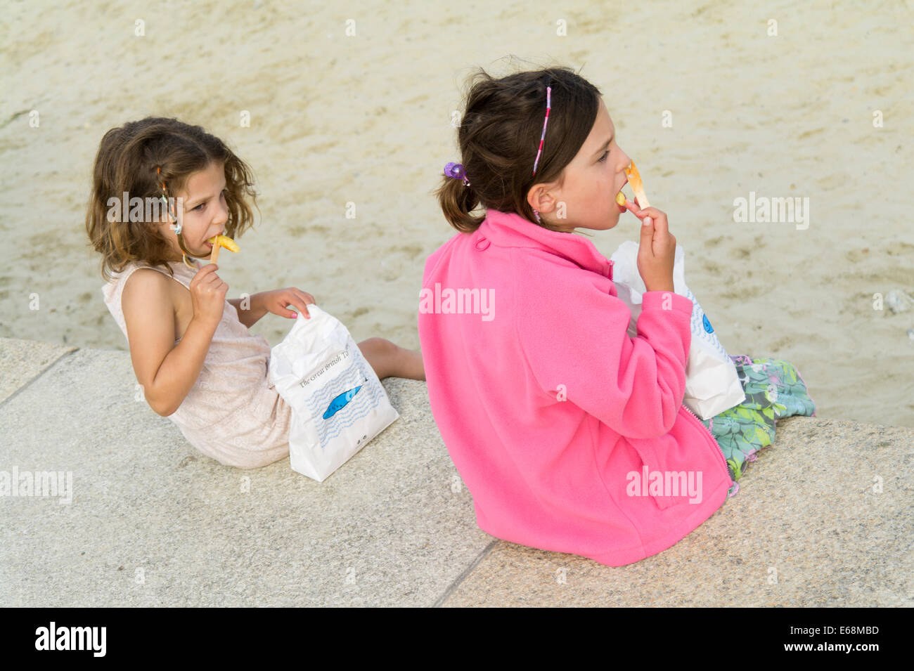 Children at beach eating fish and chips takeaway food. Stock Photo