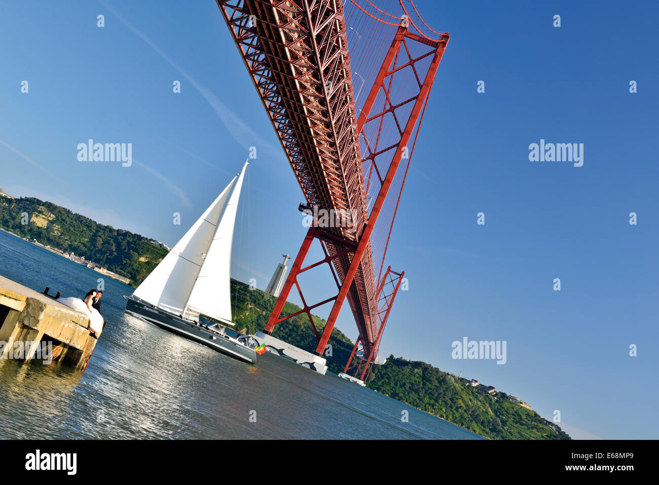 Portugal, Lisbon: Sailing boat crossing the bridge Ponte 25 de Abril Stock Photo