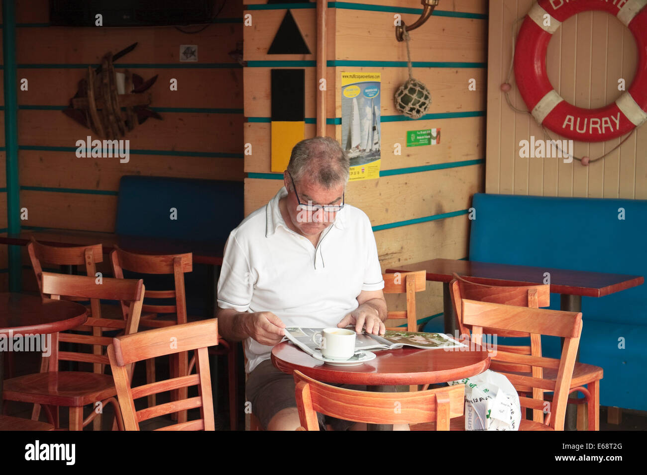 A caucasian male sitting drinking a coffee and reading a newspaper in a bar tabac in La Trinité-sur-Mer, Brittany, France Stock Photo