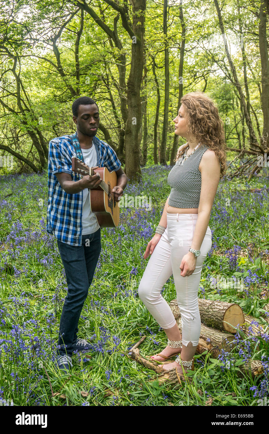 Interracial couple. A pretty teenage girl singing with her handsome boyfriend playing guitar. Banstead Woods, Banstead, Surrey, England, UK. Stock Photo