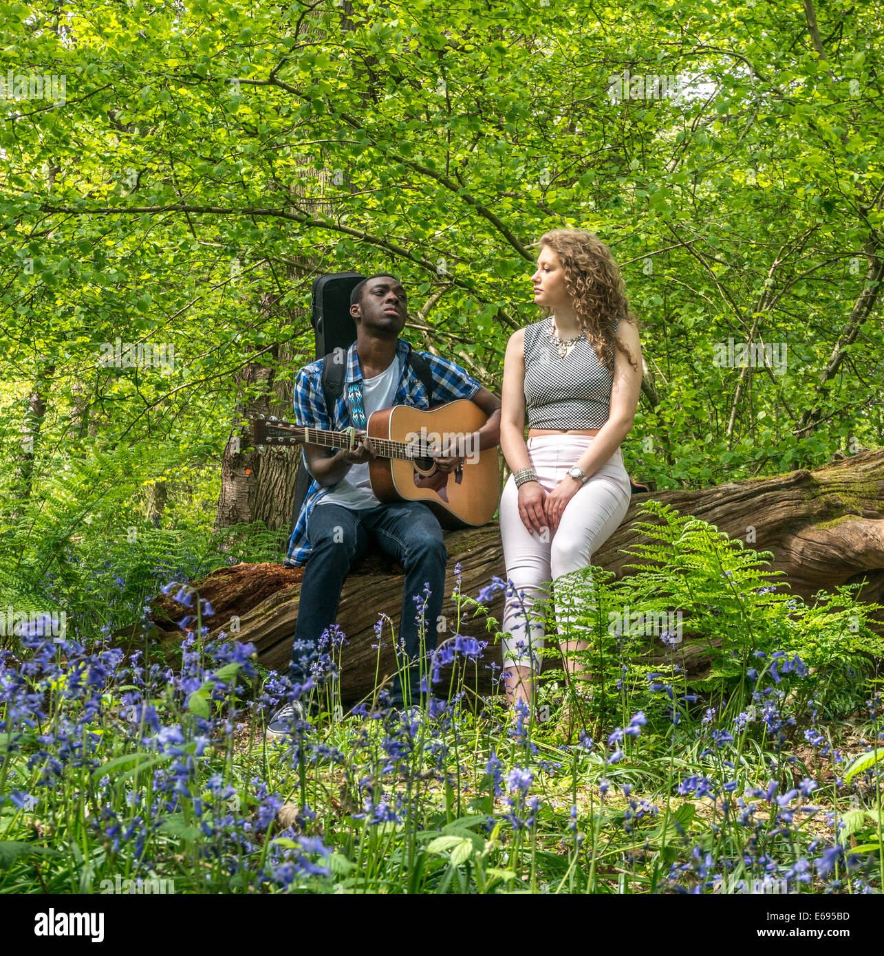 Interracial couple. A pretty teenage girl singing with her handsome boyfriend playing guitar. Banstead Woods, Banstead, Surrey, England, UK. Stock Photo