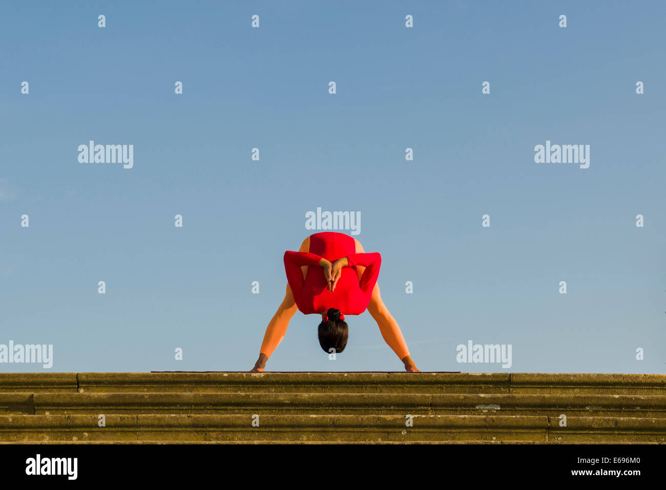 Young woman practising Hatha yoga, outdoors, showing the pose Prasarita Padottanasana, wide legged forward bend Stock Photo