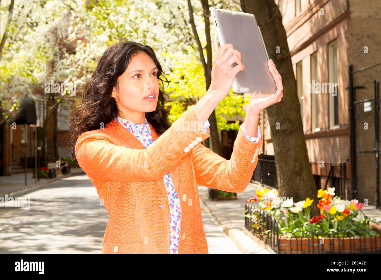 Mixed race woman taking picture with tablet computer on city street Stock Photo