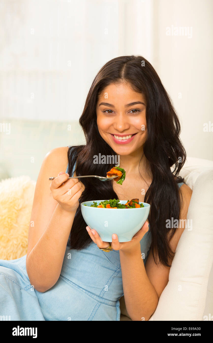 Hispanic woman eating salad on sofa Stock Photo
