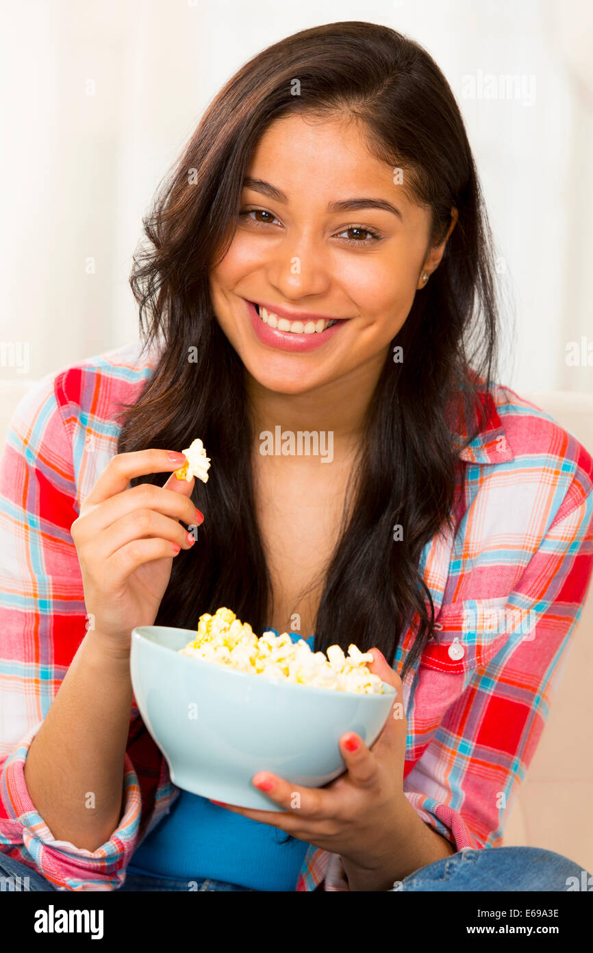 Hispanic woman eating popcorn on sofa Stock Photo