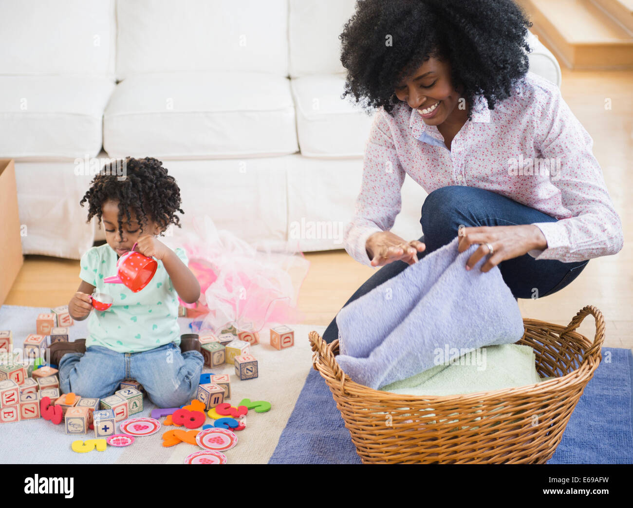 Mother folding laundry while daughter plays Stock Photo
