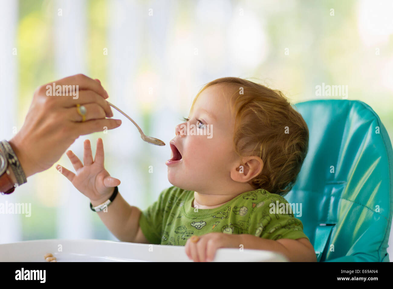 Caucasian mother feeding baby in high chair Stock Photo