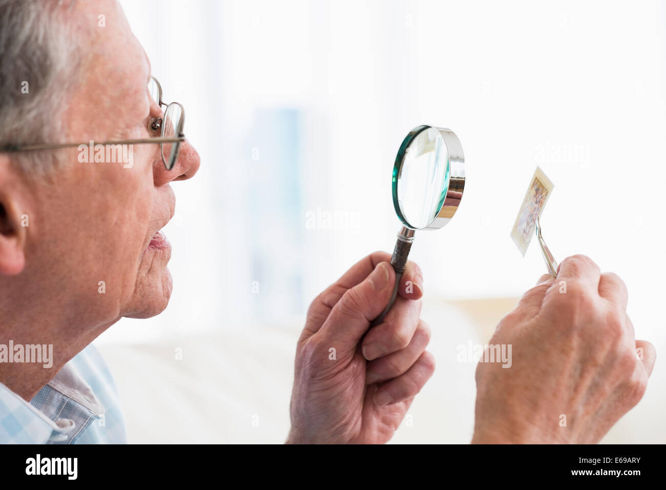 Senior Caucasian man examining stamp with magnifying glass Stock Photo